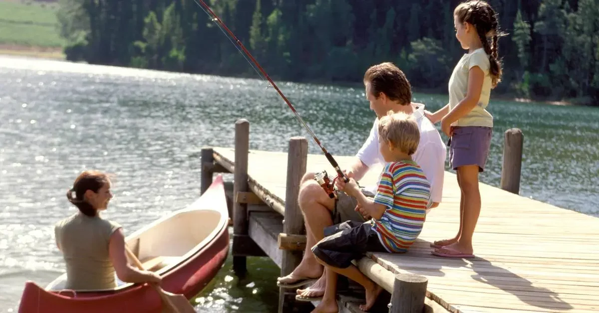 NEVEREST Freizeitpädagogik zwei Kinder am Steg mit Vater der fischt und Mutter die Kanu fährt