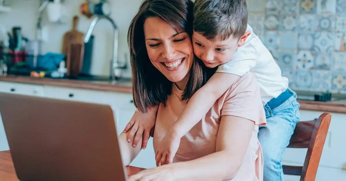 NEVEREST Home Office Mutter sitzt mit Kind auf den Schultern vor Laptop