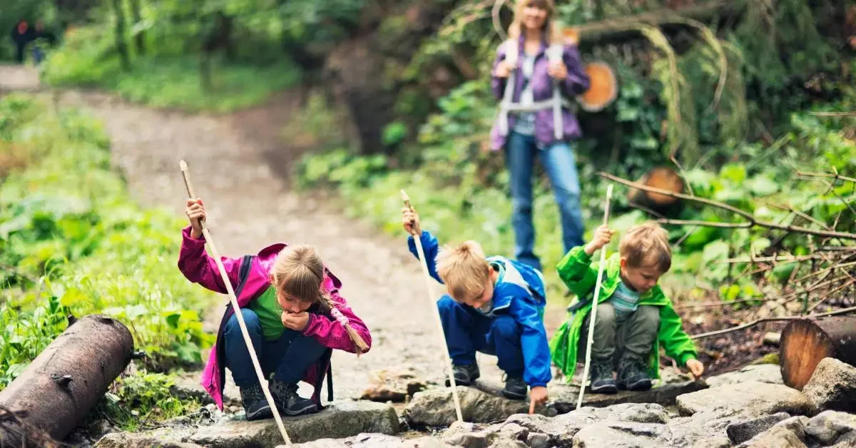 NEVEREST Waldpädagogik § Kinder untersuchen den Boden, eine Frau steht im Hintergrund